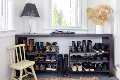 Open organized shoe cabinet in hallway with small wooden chair and decorative lamp