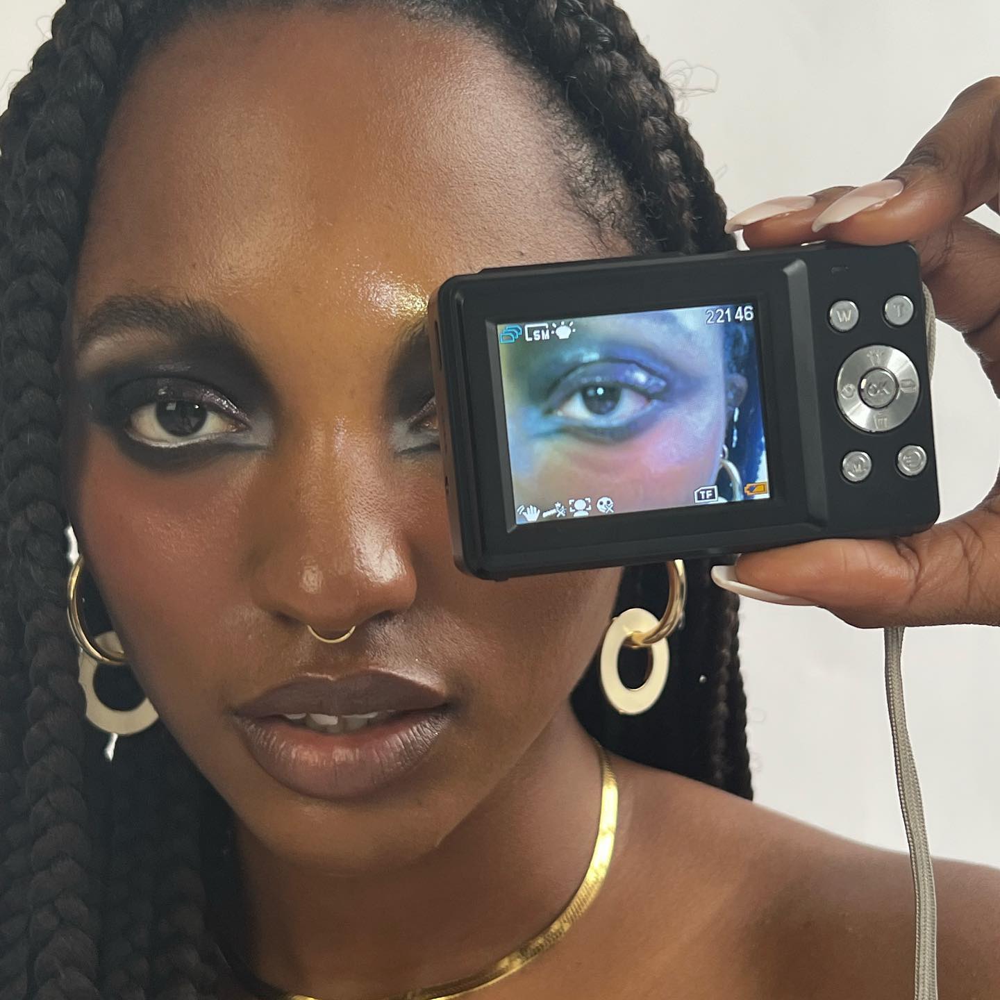 An image of a woman with heavy eye makeup and a digital camera in front of one eye.