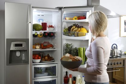 A woman looking in an open fridge filled with food and drinks in a home kitchen