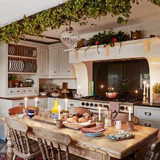 a farmhouse style kitchen with dining table with food and candles, a large range cooker and decorative plate rack shelving