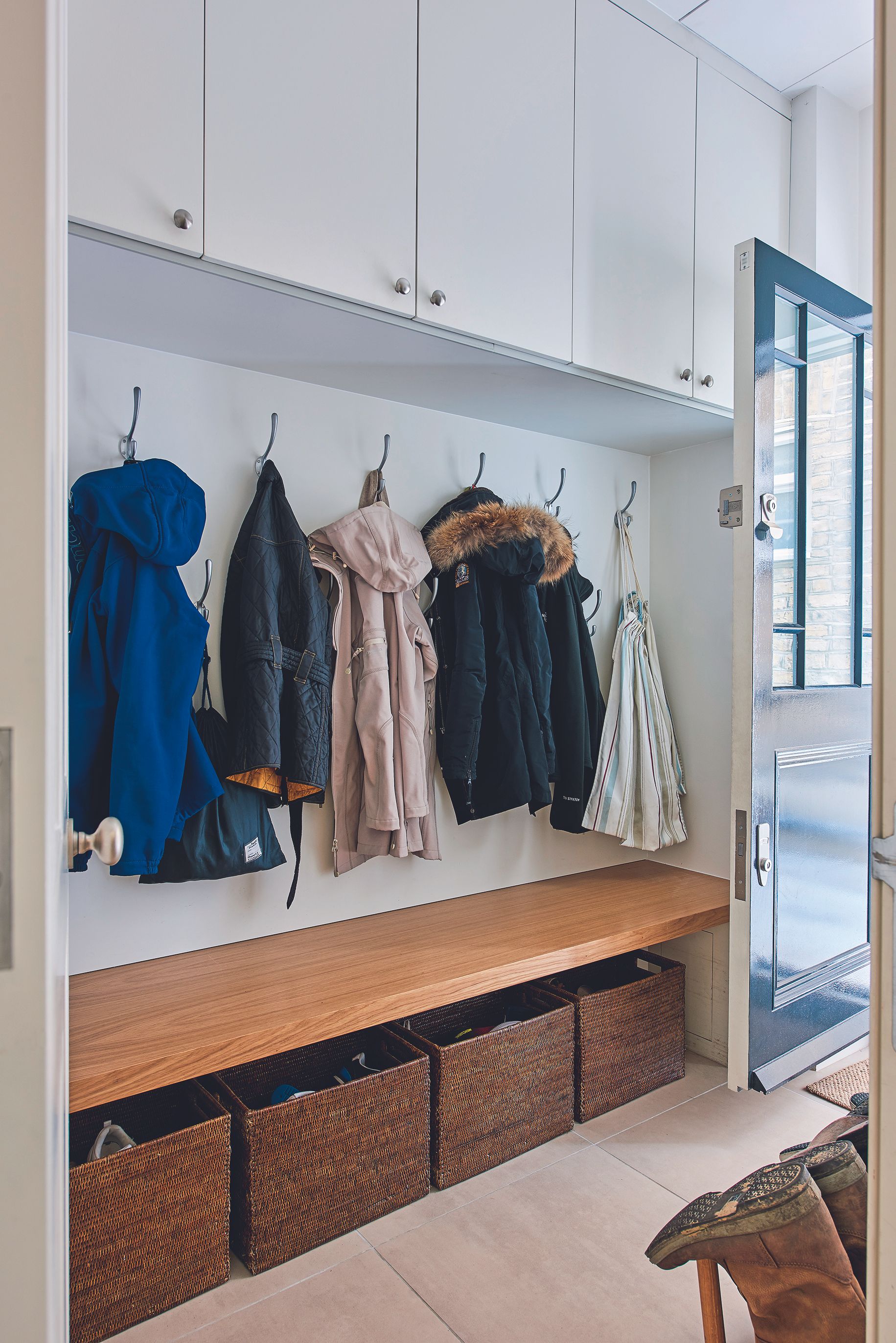 Entryway with stone floor, coats on hooks with bench and baskets below, and cabinets above