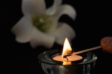 Hand lighting tea light candle with white lily in background