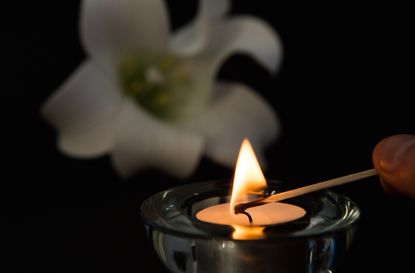 Hand lighting tea light candle with white lily in background