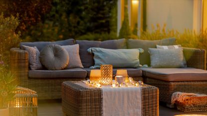 Rattan sofa with cushions on cozy patio at dusk