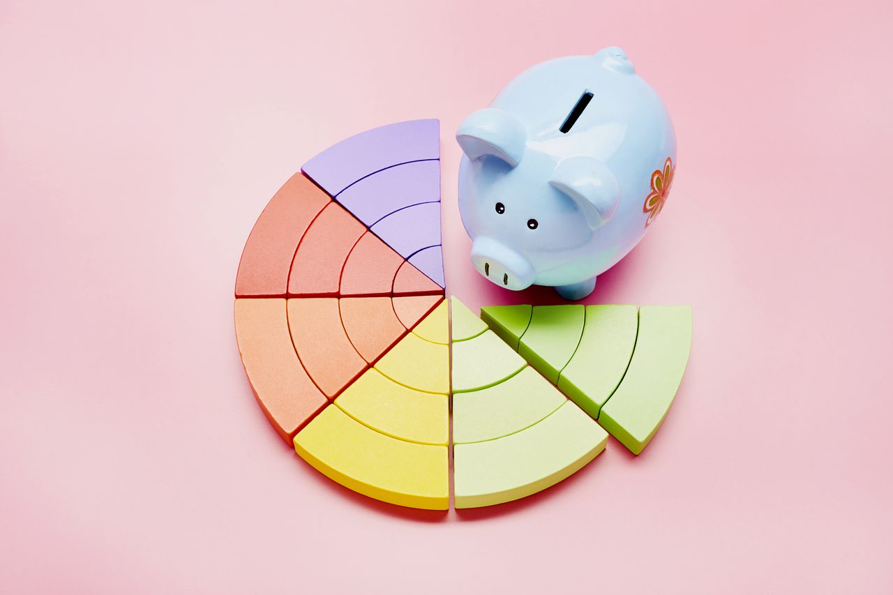 High angle view of a piggy bank and colorful pie chart on pink background