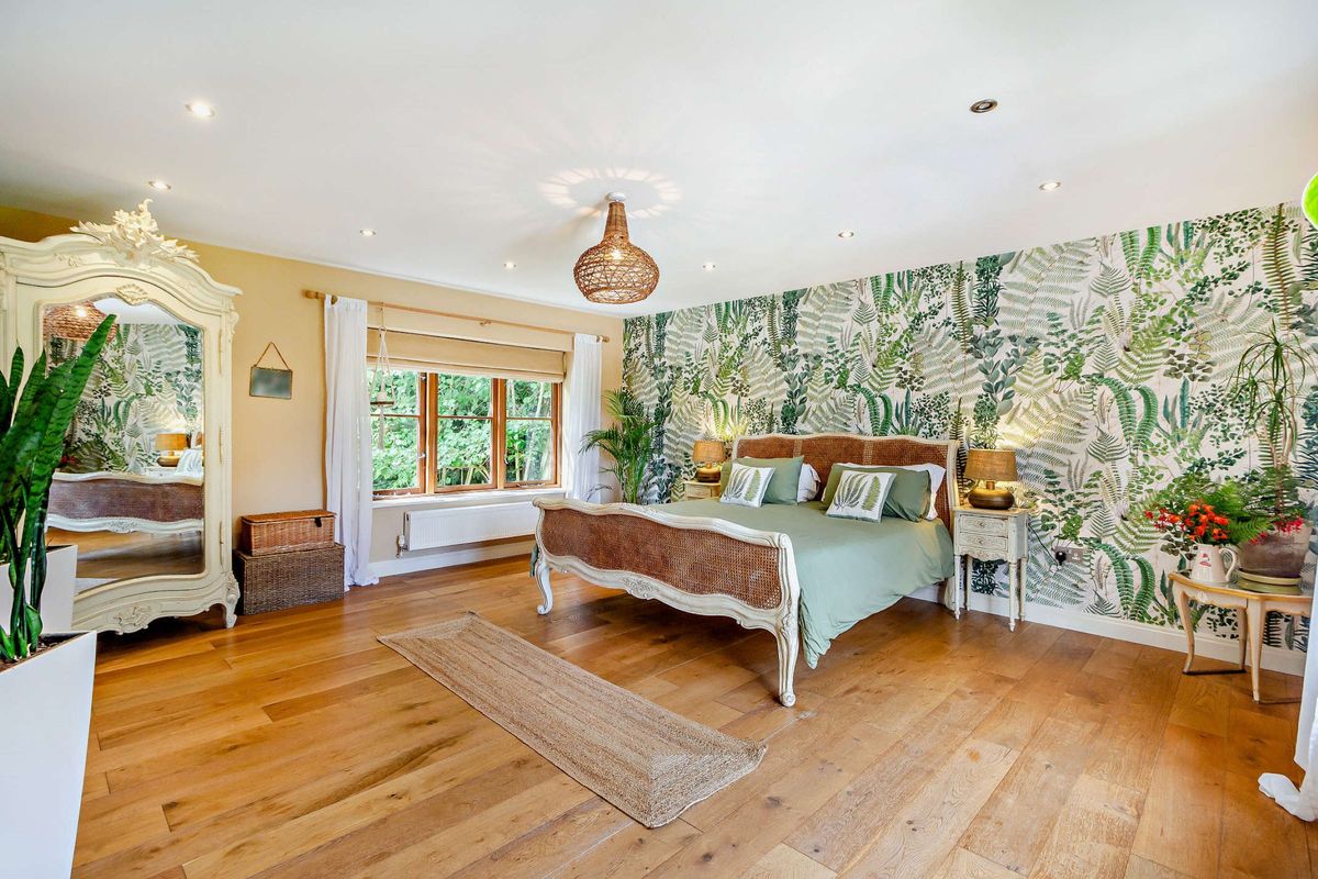 A large master bedroom with wooden flooring and green wallpaper