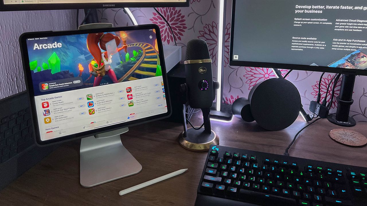 A photograph of the 12.9in Apple iPad Pro on a stand next to a monitor and keyboard