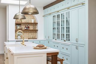 pale blue wall to ceiling kitchen units with arched alcove with open shelves and terracotta tiled backsplash and white topped island brass faucet and metal pendant lamps