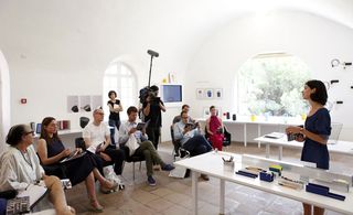A workshop led by a woman standing with the audience sitting and a camera man recording the session