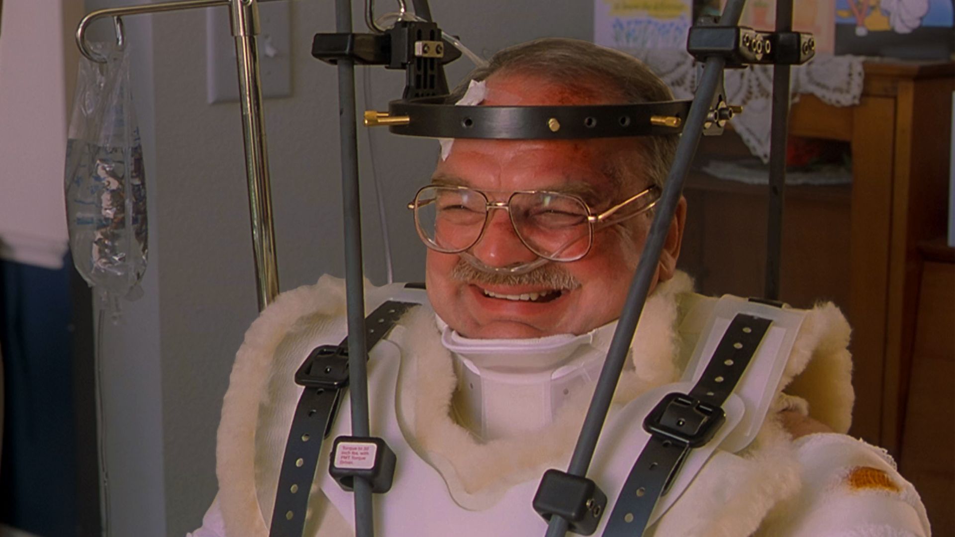Richard Riehle in a head brace, wheelchair and body cast after getting hit by a car in Office Space (1999).