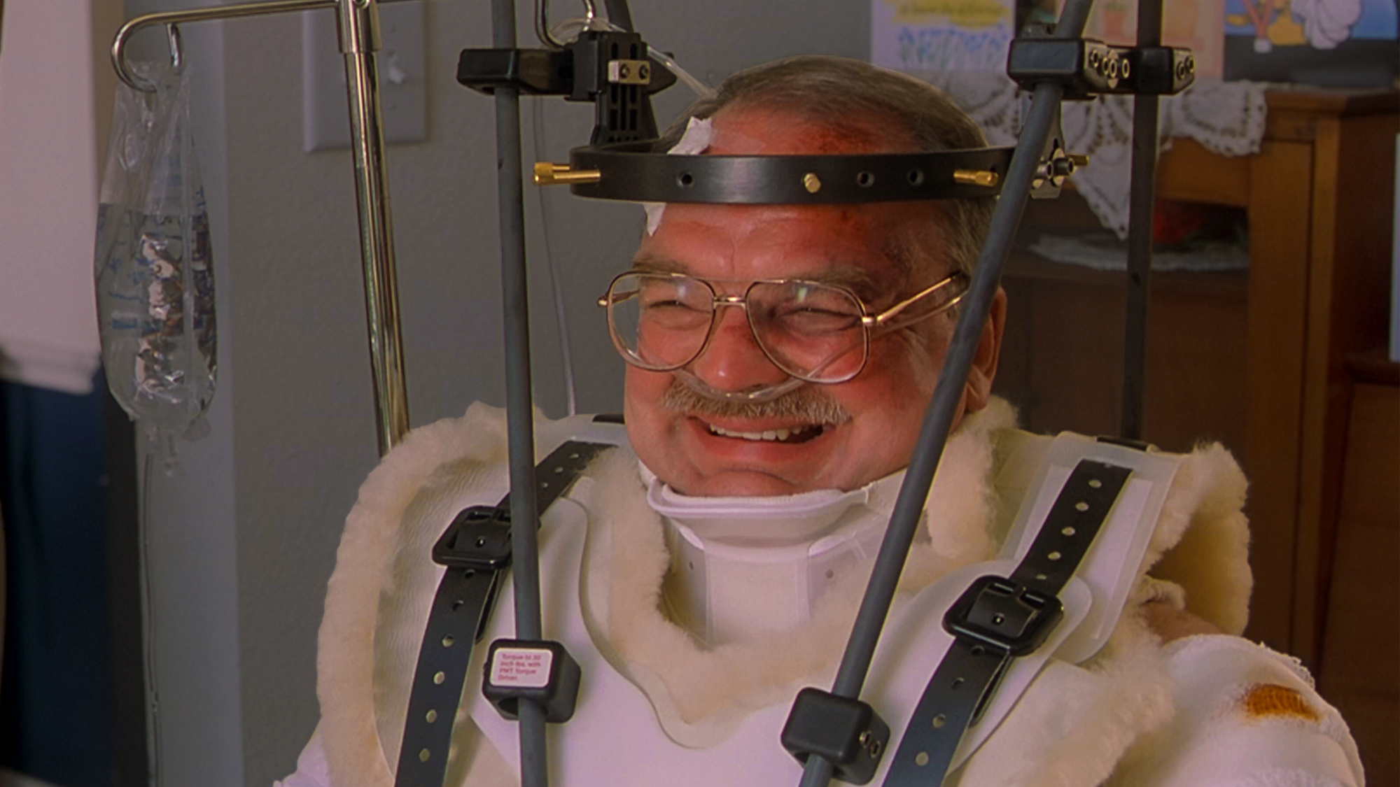 Richard Riehle in a head brace, wheelchair and body cast after getting hit by a car in Office Space (1999).