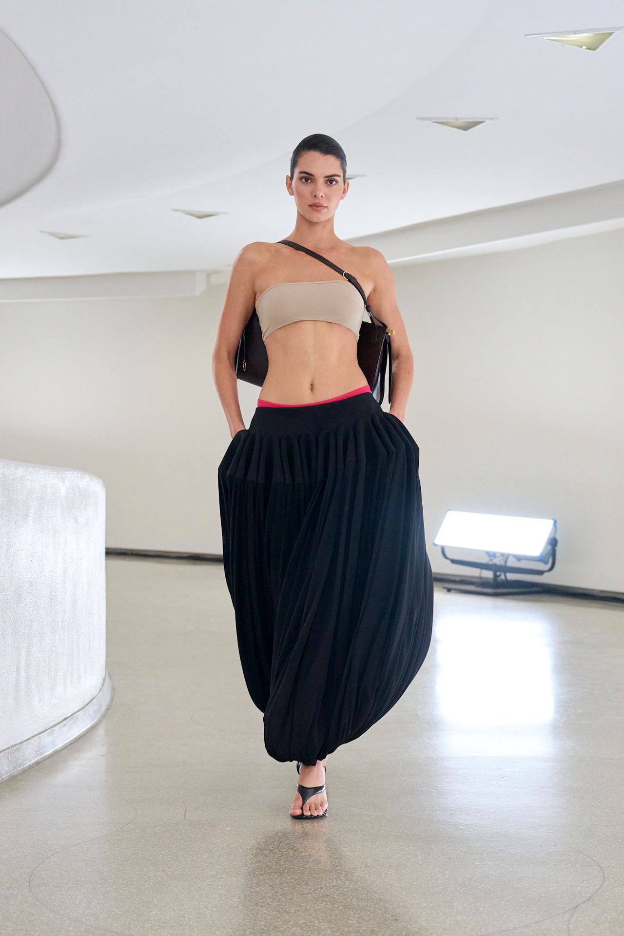 Kendall Jenner is wearing a bandeau top and black genie pants on the runway at Ala&iuml;a's spring/summer 2025 show.