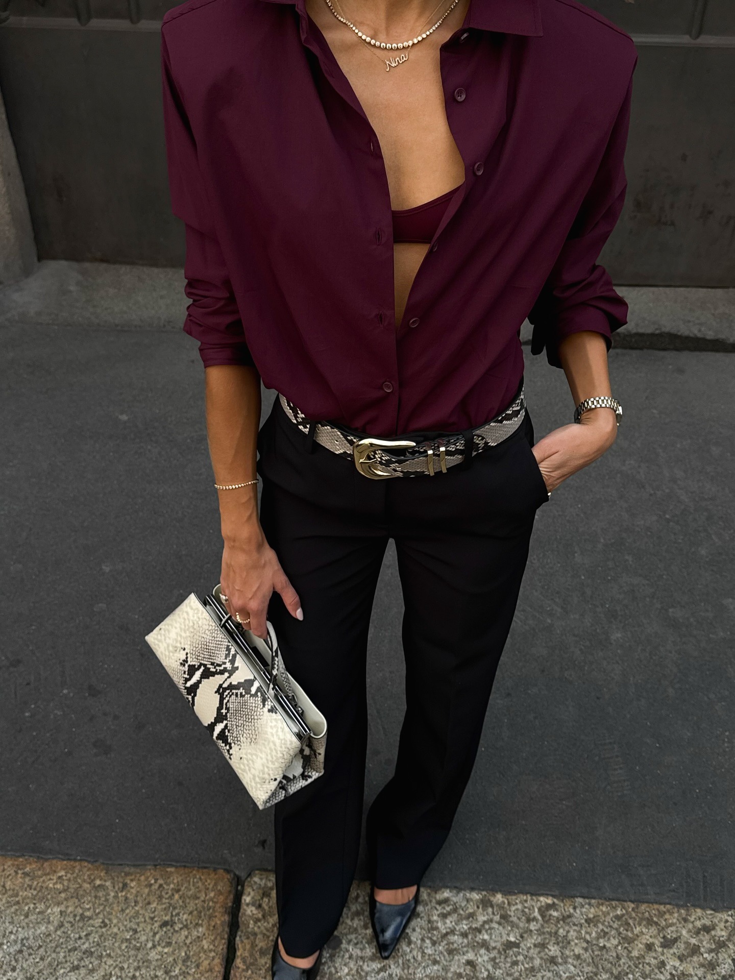 Nina Sandbech holding a top-handle snake-print white bag against black pants.