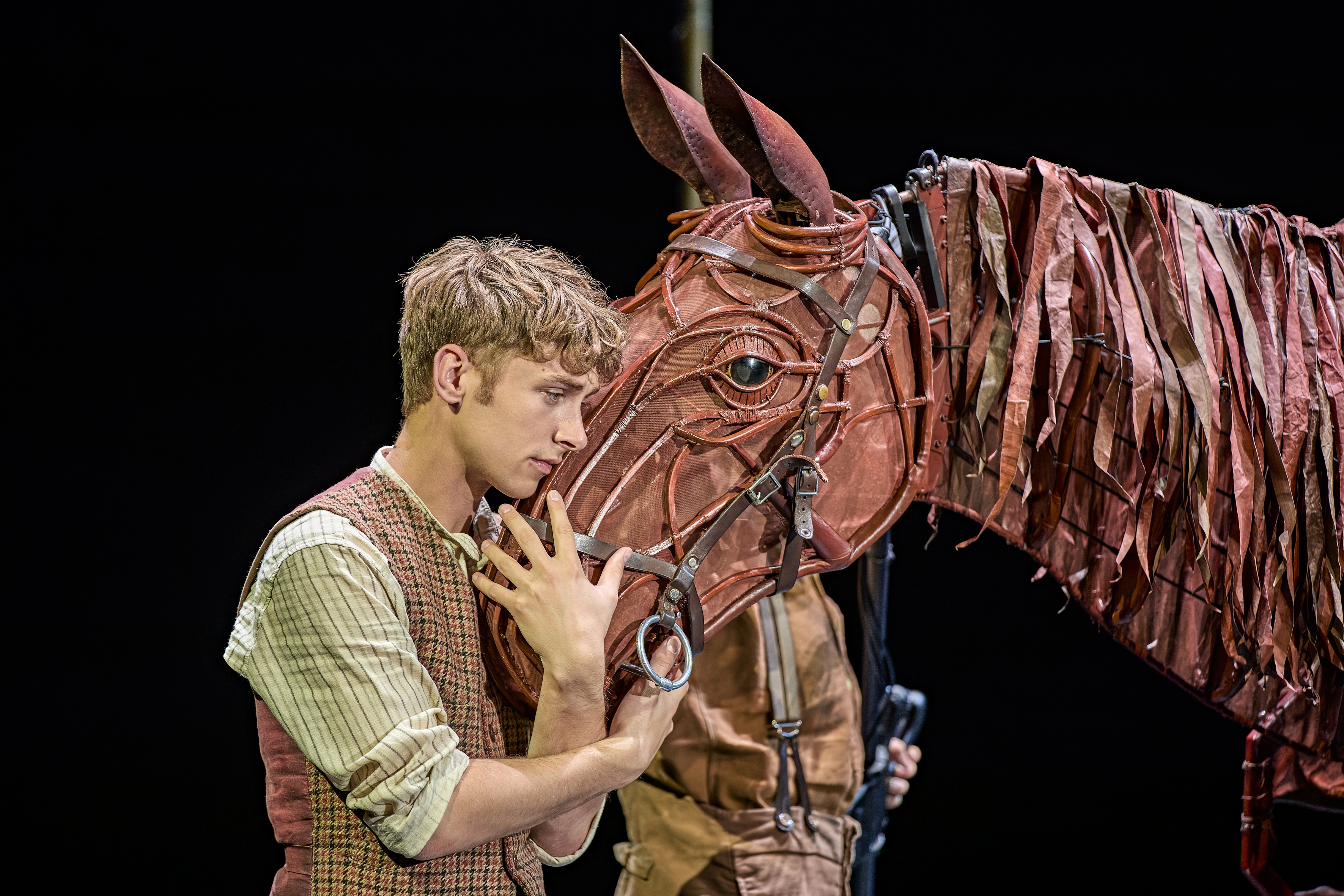 Actor Tom Sturgess embraces the life-sized puppet horse on stage in War Horse, 2026