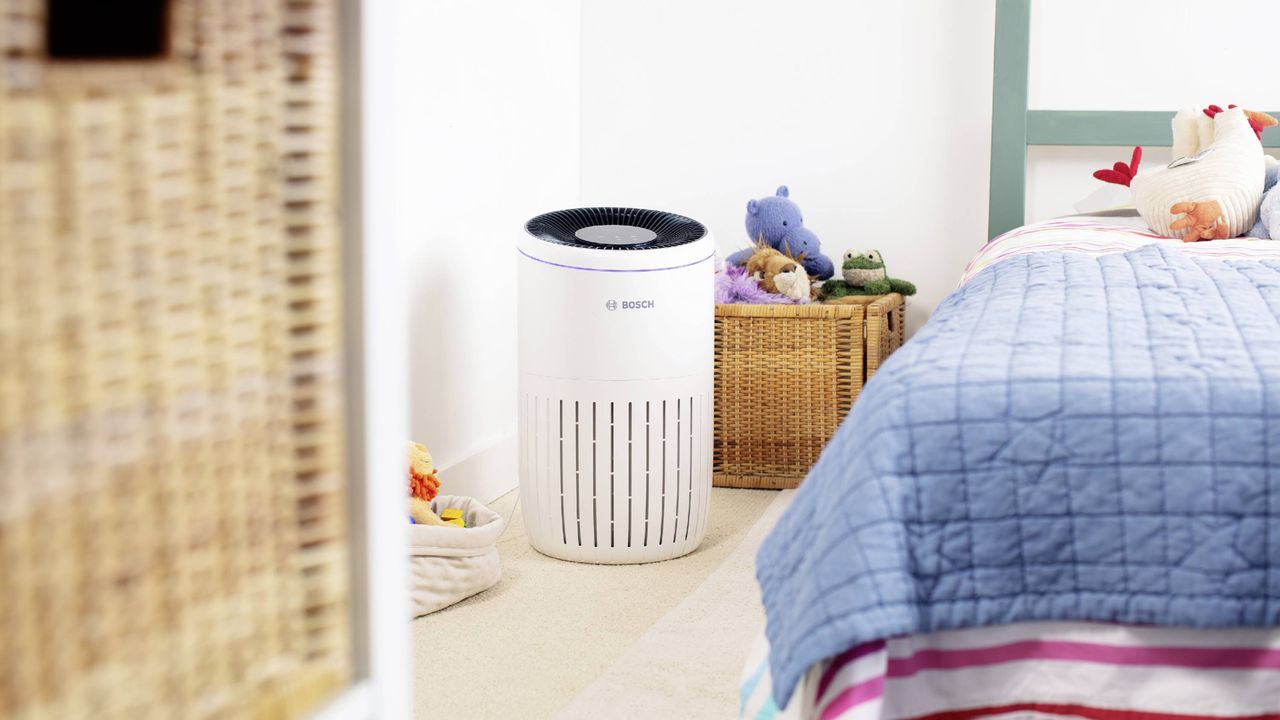 A white Bosch air purifier in a children&#039;s bedroom by the side of bed with striped red and white bedding