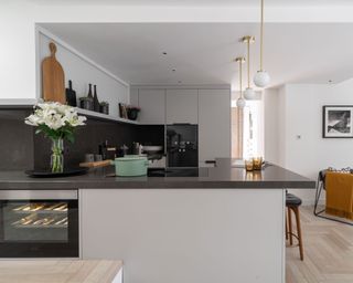 A u-shaped kitchen peninsula with black worktops and off-white cabinets below three spherical white pendant lights
