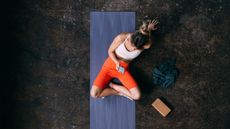 Woman seen from above sitting on yoga mat looking at smartphone with a cork yoga block next to her
