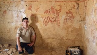 A man poses in front of a wall painting on a tomb