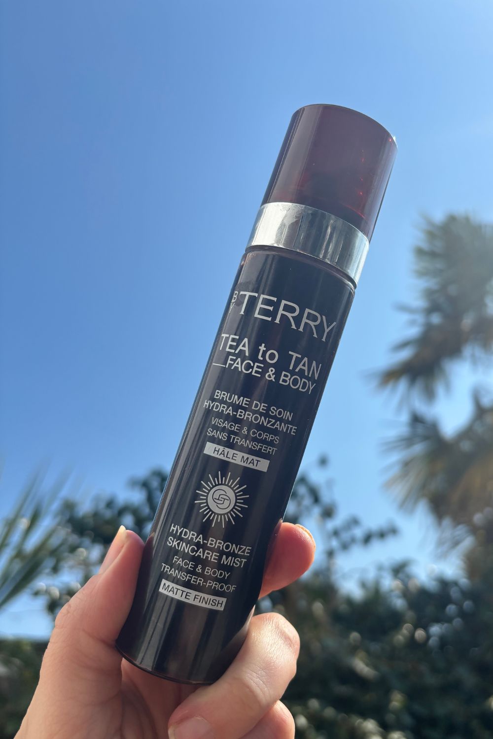 a hand holding a bottle of by terry tea to tan face & body