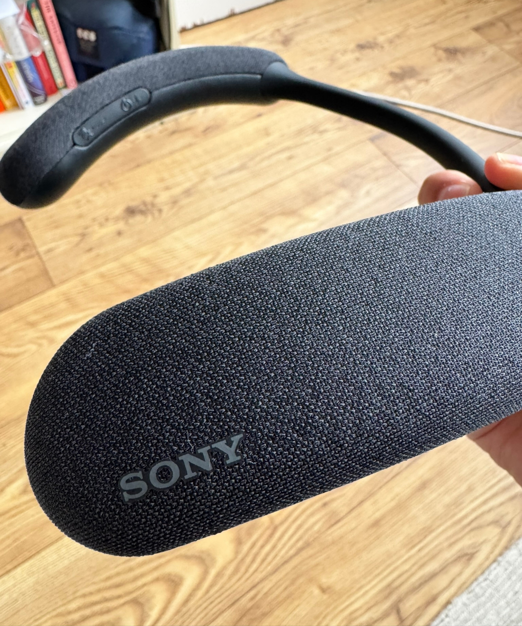 Sony BRAVIA Theater U held above wooden floor, with bookcase partially visible in background.