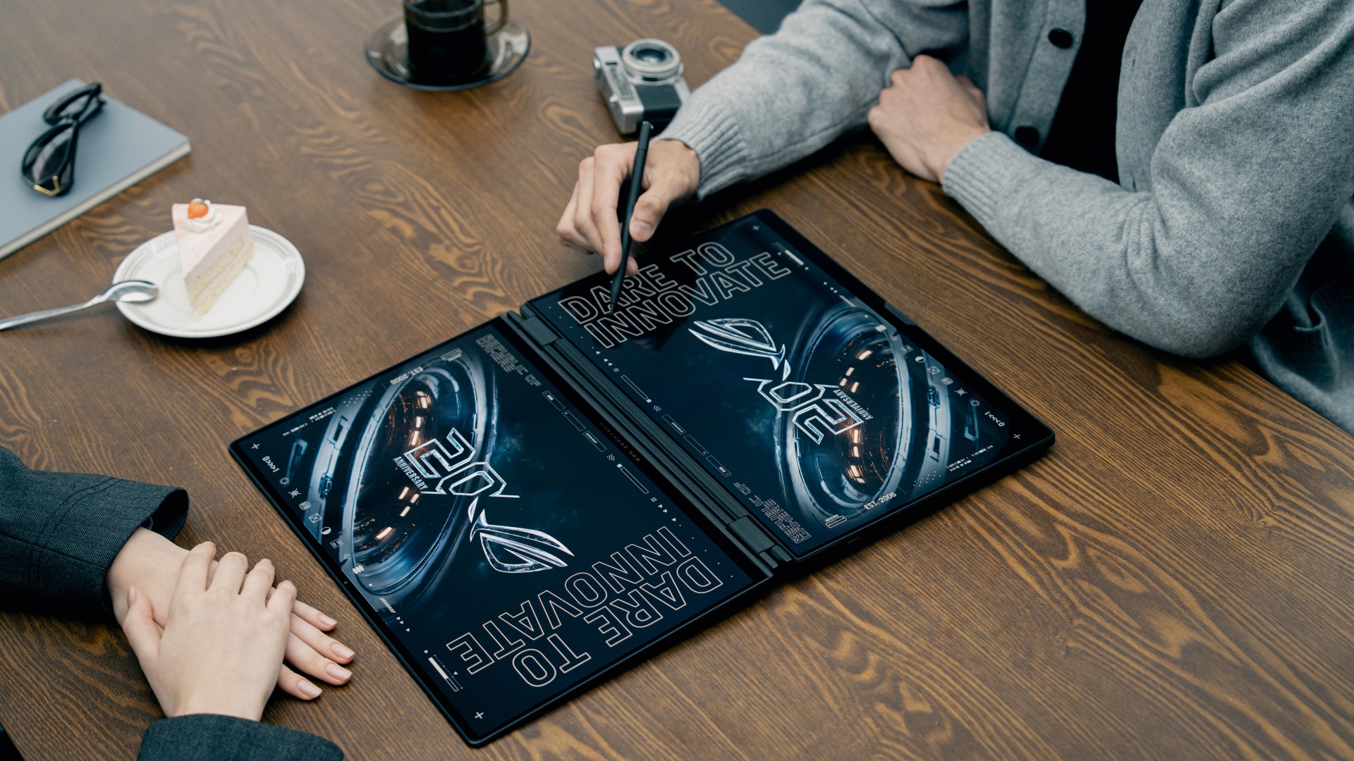 Asus ROG Zephyrus Duo laptop on a wooden desk with two users sitting each side of it