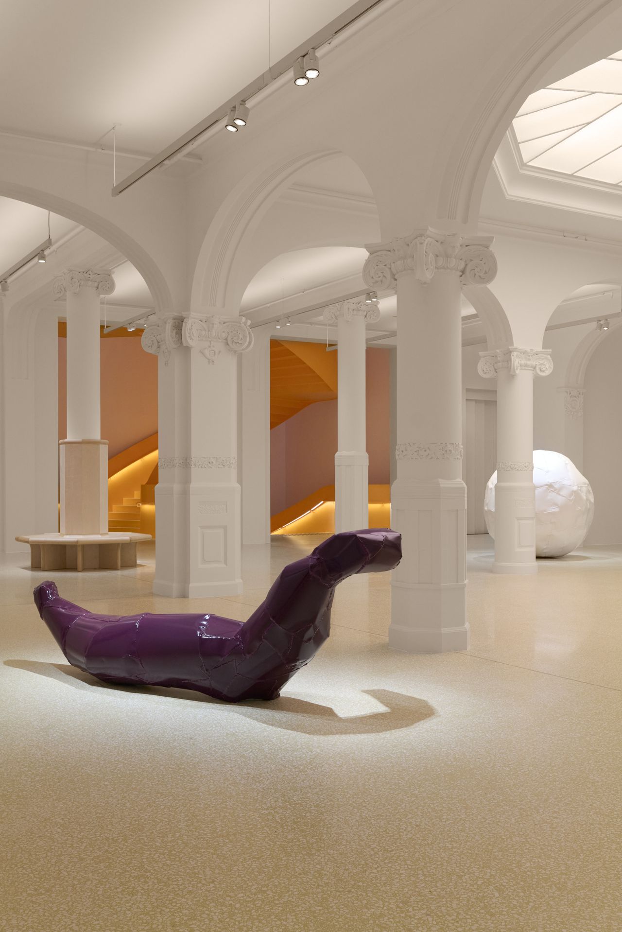 A purple snake-shaped sitting sculpture stands in an otherwise semi-bare white room with columns and arches.