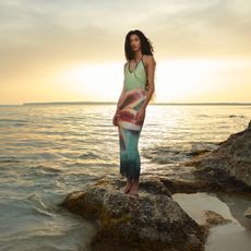 a model poses on rocks in the ocean wearing a floral maxi dress