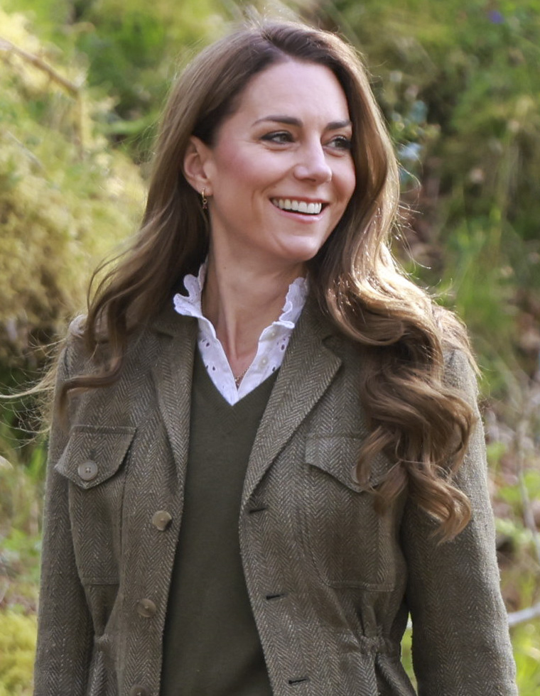 Princess Kate wearing a green sweater and tweed jacket turning to the right and smiling