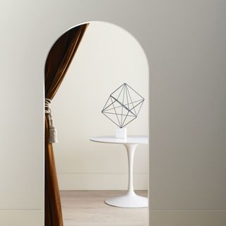 arched doorway with warm light gray walls, white table in next room with decorative object