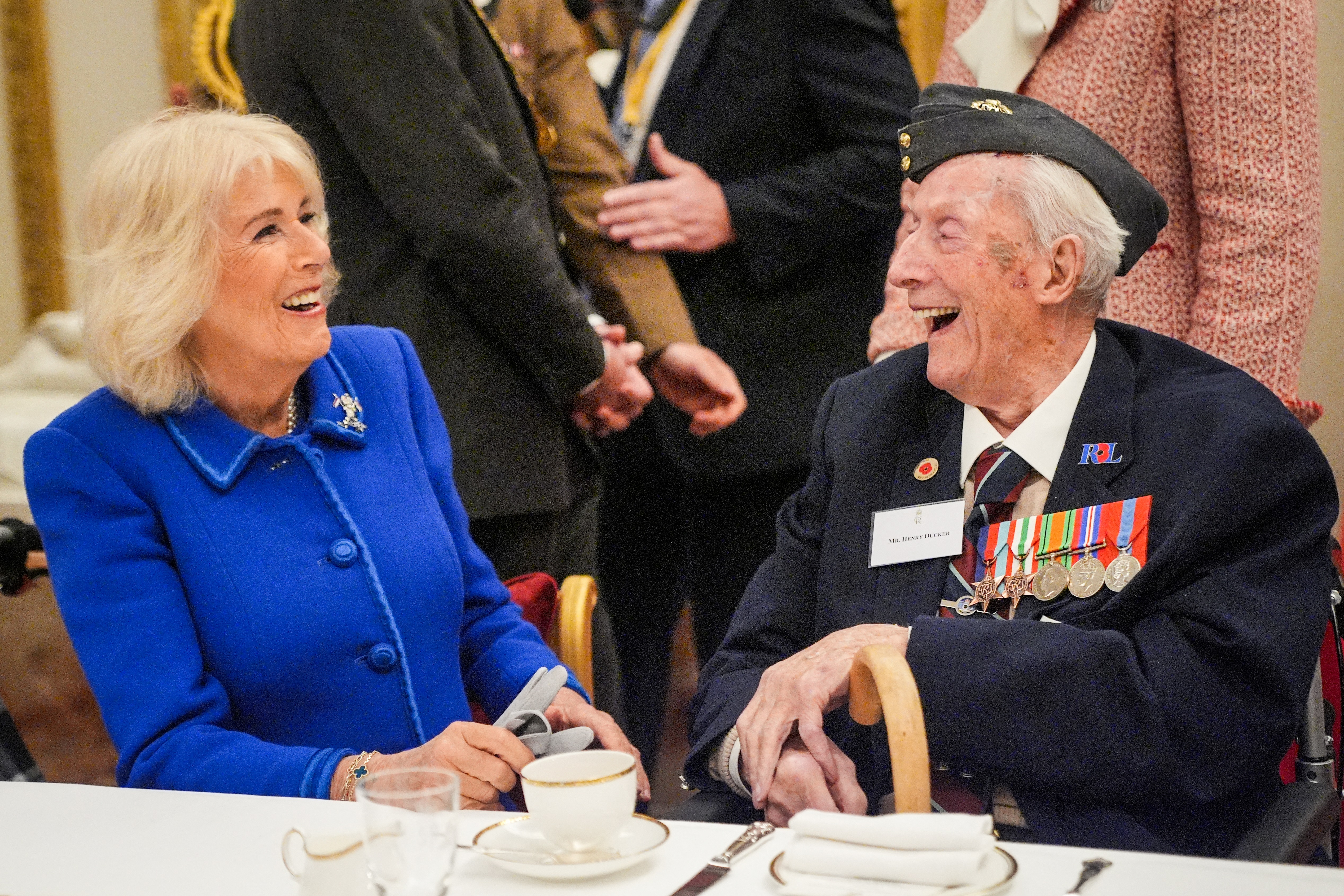 Queen Camilla laughing with a veteran at a tea party
