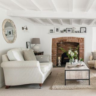 Striped linen sofa in white country living room with beams and fireplace