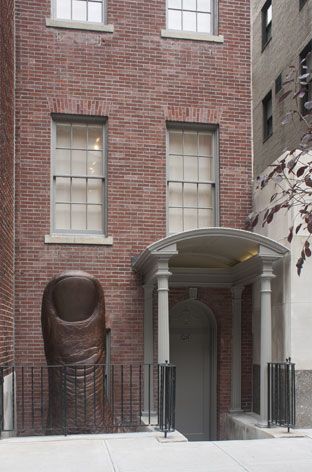 Red brick house with white porch and an eight-foot structure depicting the artist&#039;s thumb