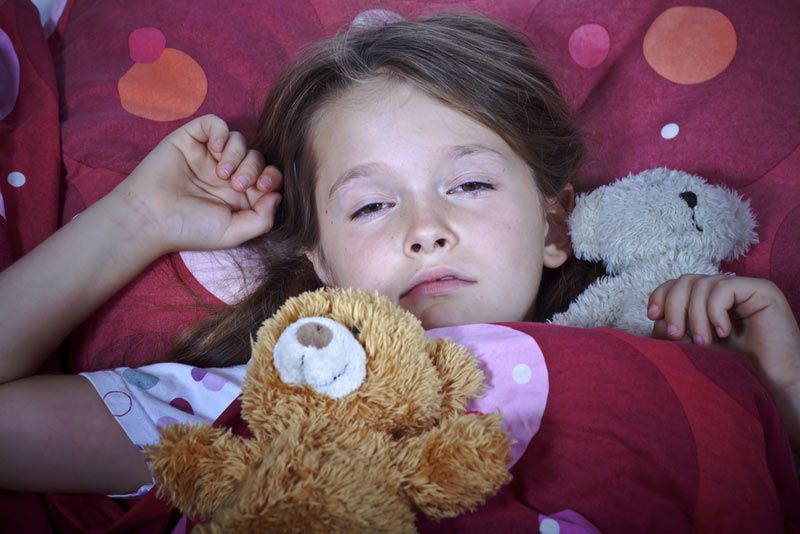 Sleepy young girl in bed holding a teddy bear.