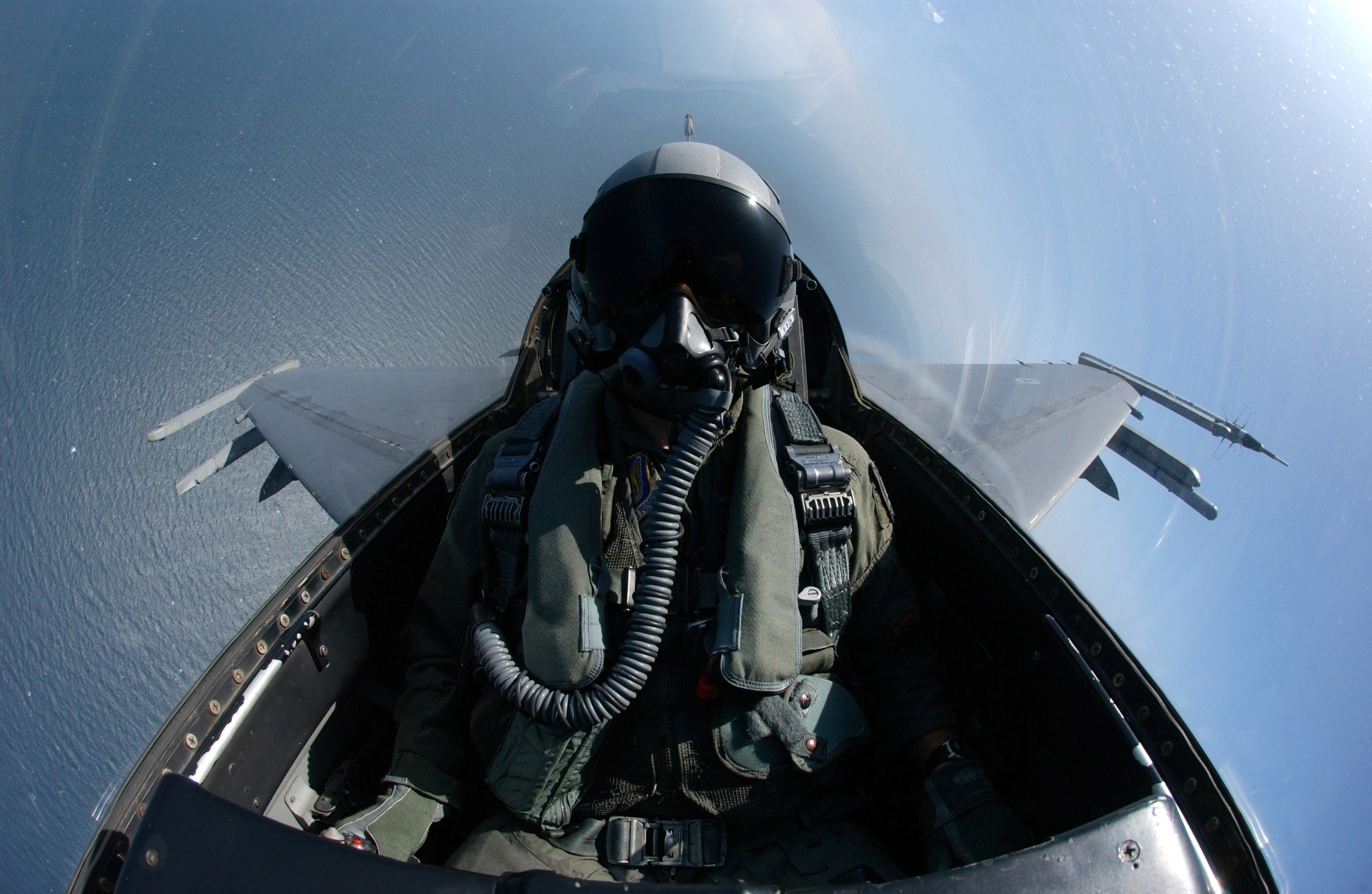 A person in a fighter jet cockpit with a view of the ocean below.
