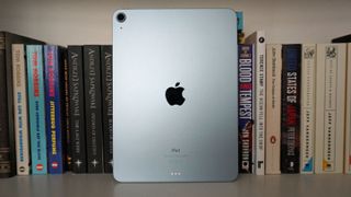 En iPad Air från 2020 står lutad mot ett par böcker i en bokhylla, med baksidan vänd mot kameran.
