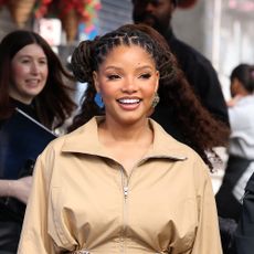 Halle Bailey wearing a tan jacket and matching skirt with white heel sandals 