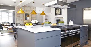 Grey blue open plan kitchen with stainless steel cooker hood over own and dining area on the other side of the L-shaped unit