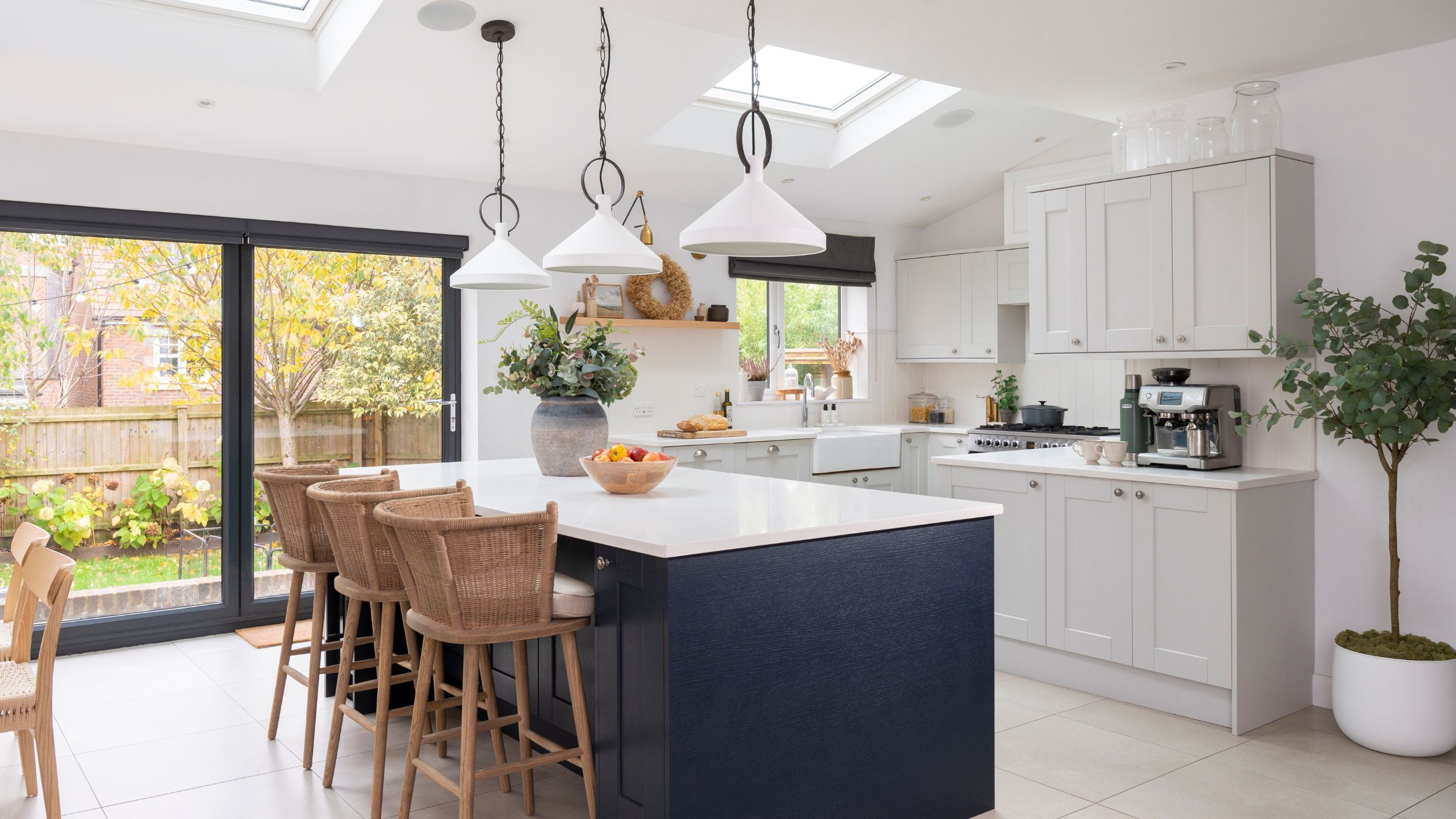 White painted kitchen with white cabinets and a large island with grey cabinets and brown wicker chairs