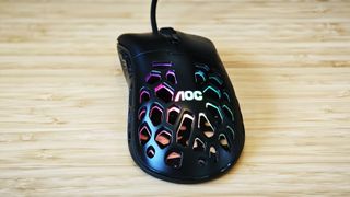 A black AOC GM510 gaming mouse with a hollow honeycomb structure and RGB lighting sitting on a desk