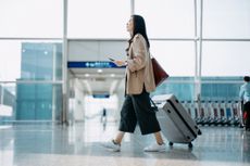 Woman walking in airport rolling suitcase getting ready to travel on an airplane.