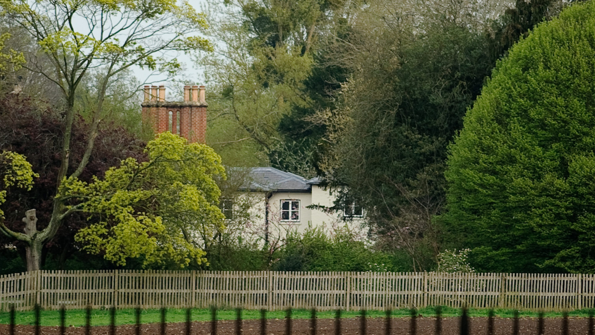 An exterior image of Frogmore Cottage along a fence and large trees