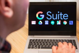 A man looks at a laptop upon which the words 'G Suite' and a series of Google service icons are displayed.