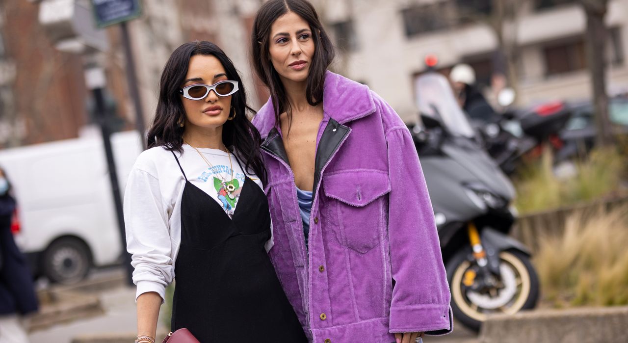 PARIS, FRANCE - MARCH 04: Amina Muaddi wearing a printed t-shirt, black dress, burgundy Loewe bag and Gilda Ambrosio wearing a purple midi dress, purple jacket and green Loewe bag, are seen outside Loewe, during Paris Fashion Week - Womenswear F/W 2022-2023 on March 04, 2022 in Paris, France. (Photo by Claudio Lavenia/Getty Images)