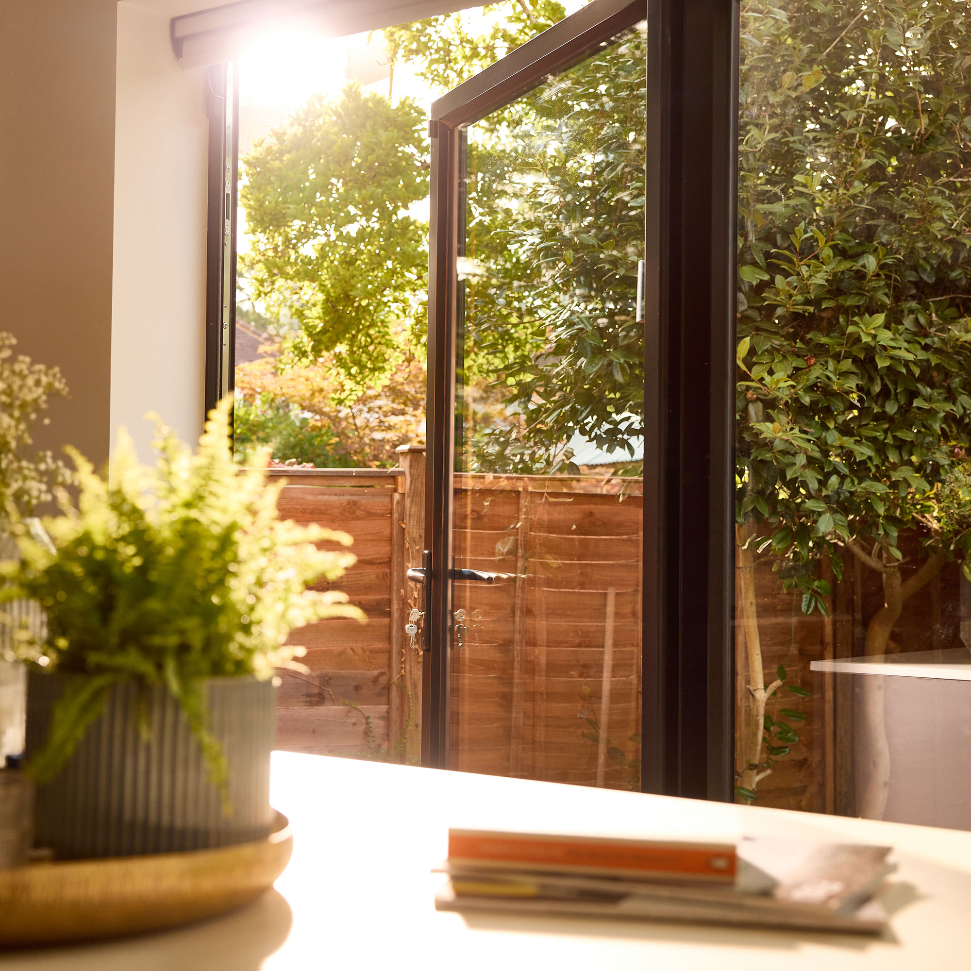 Open black framed aluminum back door leading to garden as seen across from kitchen island