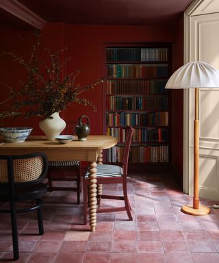 rich red dining room color drenched, terracotta tiles, floor lamp, wood table, red and black chairs, bookcase