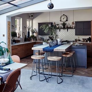 A blue and white kitchen with wooden bar stools and an open plan living space with wooden bar stools