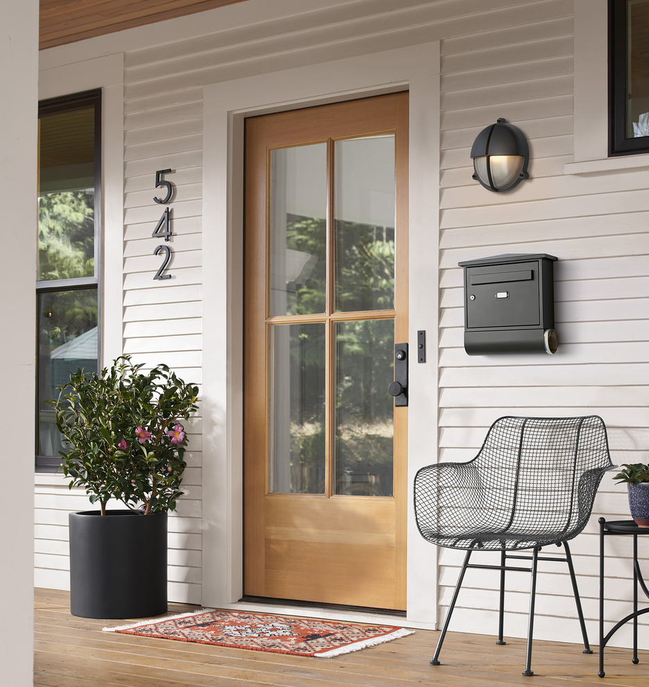 Wooden front door with four glass panels on a porch with decking and black accents
