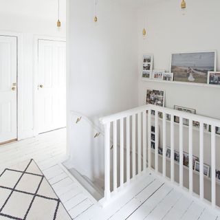 white painted floorboards and banister in landing area with rug and feature light and family photos on the wall