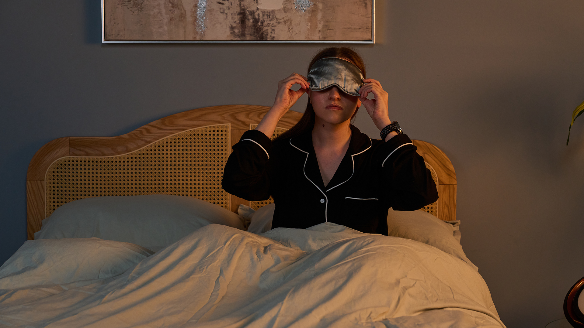 Tom's Guide senior sleep writer, Frances Daniels. sits up in bed while pulling a grey silk eye mask over her eyes to go to sleep