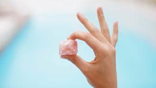 person holding a pink crystal in their hand with a pool in the background